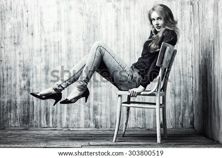 Black-and-white portrait of a beautiful blonde girl in jeans clothes posing by the grunge wall. Fashion.