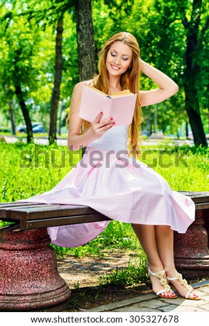 Pretty young woman reading a book sitting on the bench on a sunny summer day.