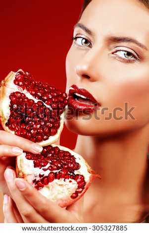 Attractive young woman eating fresh pomegranate. Sexual lips, red lipstick. Healthy food concept. Red background.