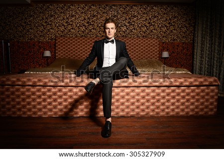 Handsome man in elegant suit sitting on a bed. Luxury. Vintage interior.