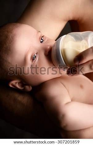 Caring father feeding his baby from a bottle. Healthy baby food and infant formula, milk. Studio shot over black background.