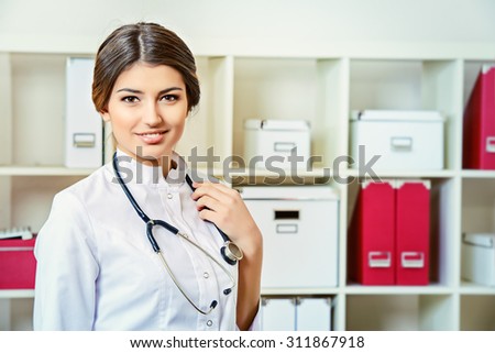Portrait of a kind woman doctor standing in her consulting room with a stethoscope and smiling at the camera. Healthcare, medicine.