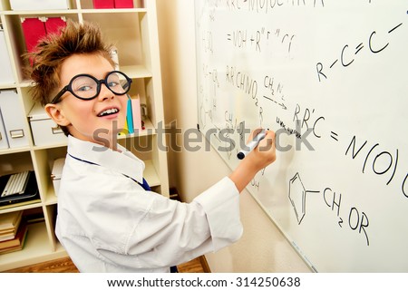 Funny schoolboy in big glasses standing by the school board. Chemistry. Science and education.