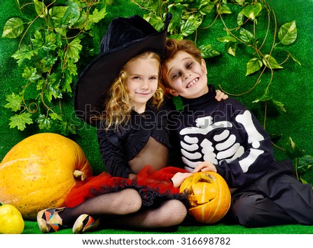 Funny boy and a girl wearing halloween costumes posing with pumpkins. Halloween.