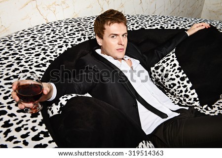 Handsome young man in elegant suit with glass of beverage relaxing. Party.