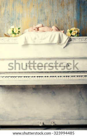 Little newborn baby sleeps on a white piano. Vintage style. Music, art concept.