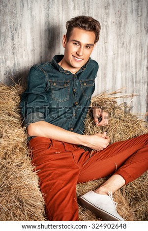 Casual young man lying relaxed on a haystack. Jeans style. Male fashion.
