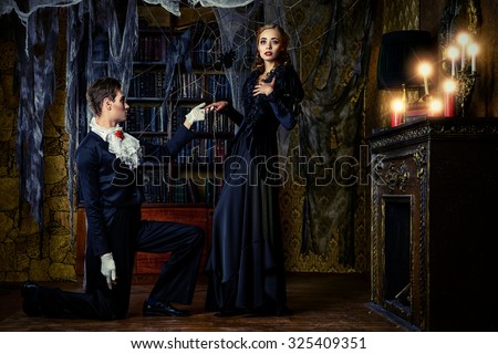 Beautiful man and woman vampires dressed in medieval clothing stand in a room of the old abandoned castle. Halloween.