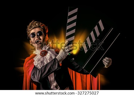 Portrait of a extravagant vampire with a clapper board. Halloween. Cinema industry.