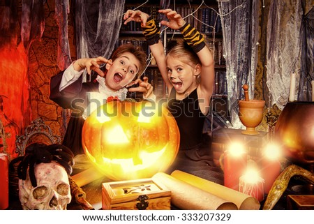 Two cute children dressed as a vampire and a black cat posing with pumpkin in a halloween room. Halloween concept.