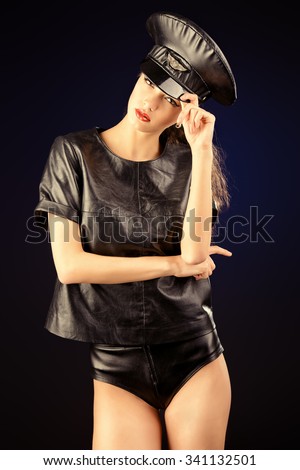 Sexual young woman alluring in fitting leather suit and a cap of police officer. Beauty, fashion.