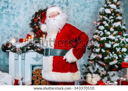 Traditional Santa Claus standing by the fireplace and Christmas tree in a beautiful room, decorated for Christmas.