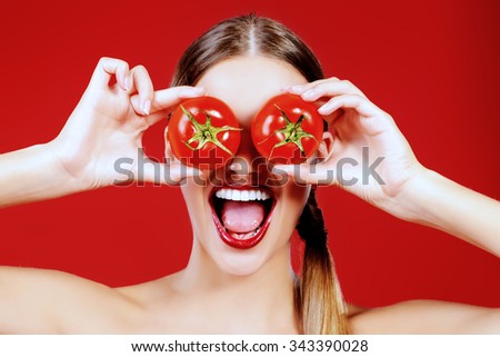 Beautiful laughing woman holding two ripe tomatoes before her eyes. Red background. Healthy eating concept. Diet.