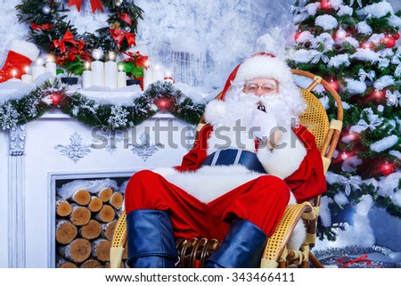 Traditional Santa Claus sitting in a rocking chair in the room by the fireplace and Christmas tree and smokes a pipe.