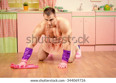 Handsome muscular man in an apron mopping the floor in the pink kitchen. Love concept. Valentine\'s day.