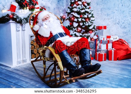 Good old Santa Claus sitting in a rocking chair in the room by the fireplace and Christmas tree, beautifully decorated for Christmas.