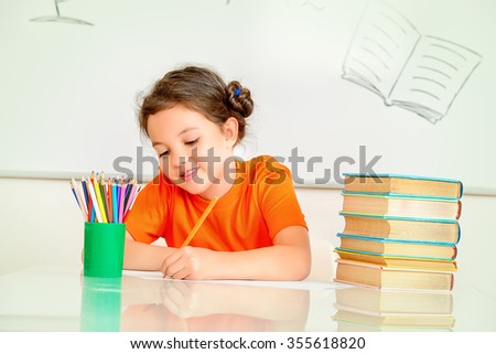 Pretty smart schoolgirl sitting at the desk in the classroom on blackboard background. Education.