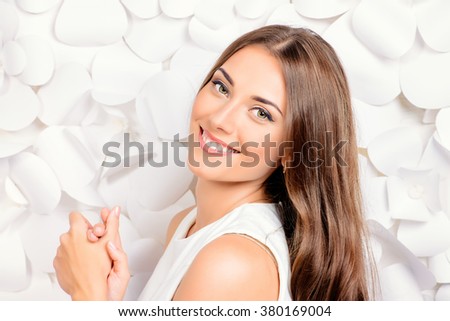 Smiling young woman in white dress posing by the background of white paper flowers. Beauty, fashion. Healthy teeth. Cosmetics.