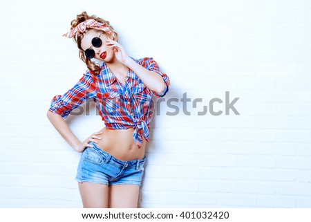 Pretty pin-up girl alluring by the brick wall in shorts and shirt. Beauty, fashion. Optics, eyewear.