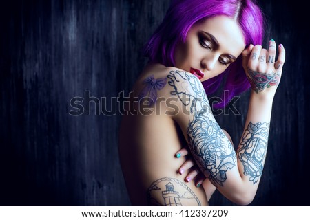 Beautiful young woman with stylish crimson hair and tattoo on her body posing over dark grunge background. Hair coloring. Cosmetics, make-up. Tattoo.