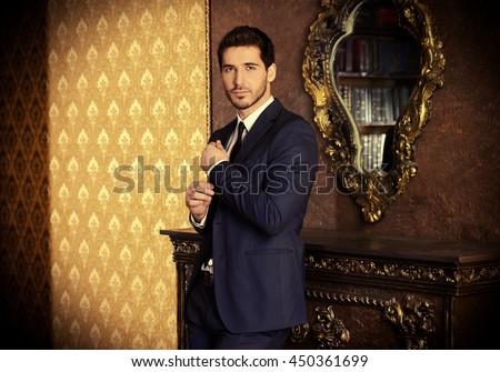Respectable young man standing by a fireplace in a room with classic interior. Luxury. Men\'s beauty, fashion.