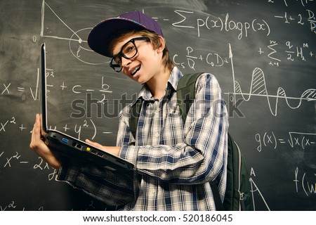 Education, high school, college. Portrait of a student boy standing by a school blackboard with his laptop.