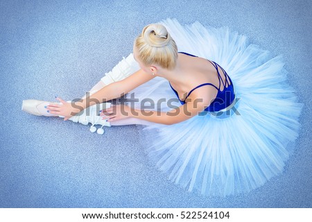 Portrait of a professional ballet dancer sitting on a floor. Female ballerina having a rest after performance or rehearsal. Ballet concept.