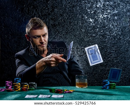 Excited gambling man throwing playing cards on a game table in a casino. Gambling, playing cards and roulette.