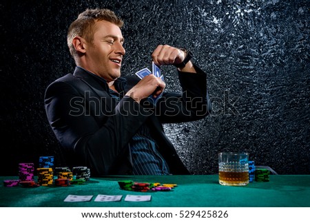 A wealthy mature man drinking brandy and playing poker with the excitement in a casino. Gambling, playing cards and roulette.