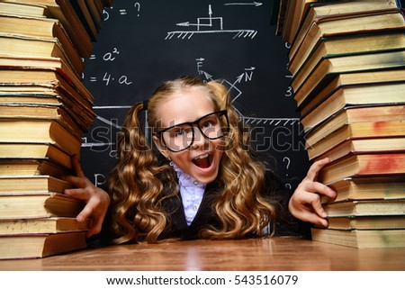 Portrait of a smart schoolgirl in glasses posing with books over school blackboard. Educational concept.