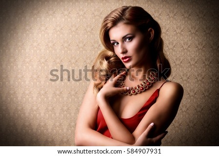 Beautiful charming woman wearing evening red dress and a necklace of gems posing over luxurious vintage background. Beauty, fashion. Evening make-up and hairstyle. Jewellery.