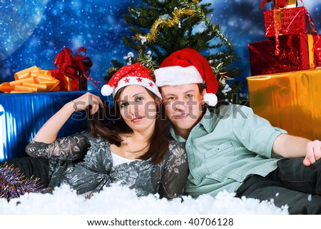 Christmas theme: happy young people in Santas caps sitting together on a snow.