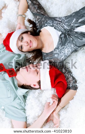 Christmas theme: happy young people in Santas caps lying on a snow together.