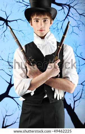 Portrait of a young gentlemen in a jacket and  top hat holding guns in his hands. Shot in a studio.