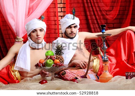 Shot of two men in oriental costumes having a rest and smoking hookah.