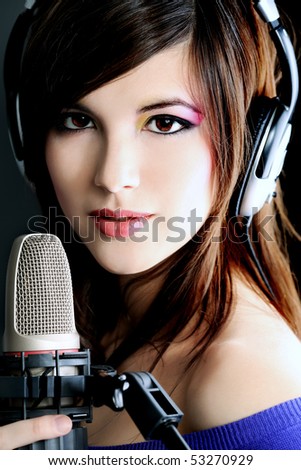 Shot of a pretty young woman in headphones singing a song with a microphone. Shot in a studio.