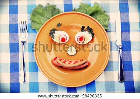 Shot of a dish with funny face made of fried sausage, egg and greens.