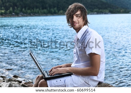 Happy young man sitting near the sea with a laptop.