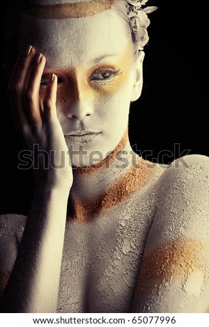 Portrait of an artistic woman painted with white and bronze colors, over black background. Body painting project.
