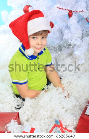 Christmas theme: little boy in santa hat sitting in snow with presents.