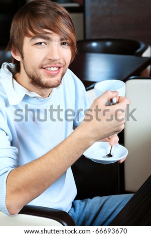 Handsome young man with a cup of tea and cake at a caf