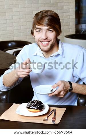 Handsome young man with a cup of tea and cake at a caf