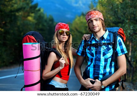 Two young people tourists hitchhiking along a road.