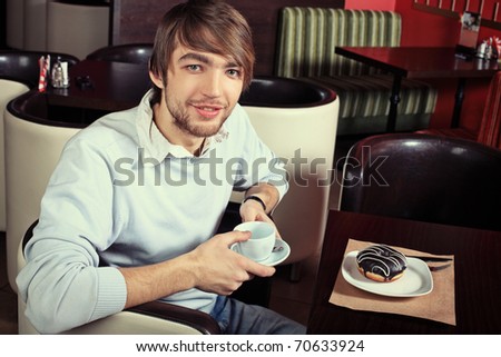Handsome young man with a cup of tea and cake at a cafe