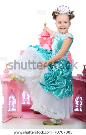 Beautiful little girl in princess dress playing with her toy castle. Isolated over white background.