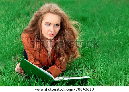 Beautiful smiling young woman reading a book outdoors.