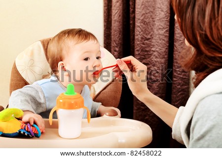 A mother is feeding her baby in the highchair at home.