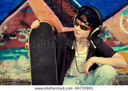 Portrait of a trendy boy teenager with headphones and skateboard outdoors.