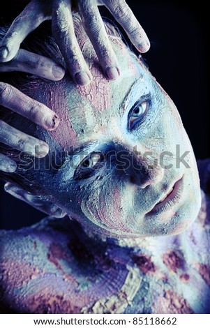 Portrait of an artistic woman painted with clay. Shot in a studio over black background.