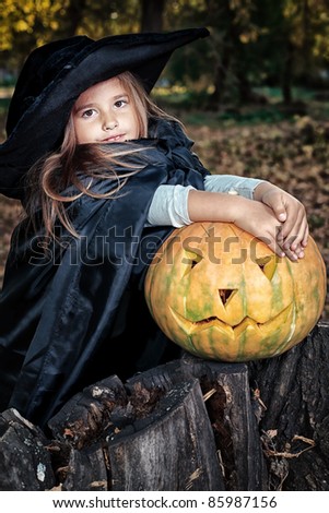Shot of a little girl in halloween costume posing with pumpkin outdoor.